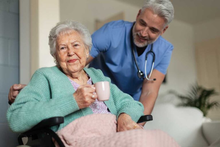 Family member visiting an older adult in an assisted living apartment, sharing conversation and holding hands.