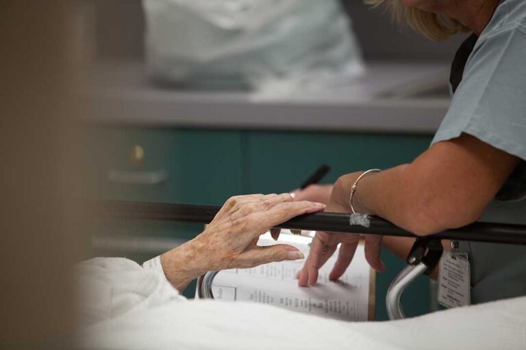 Older couple sits together in a bright assisted living apartment while a caregiver reviews a daily routine.